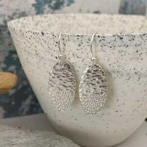 This is an image of silver earrings with a sand and sea pattern